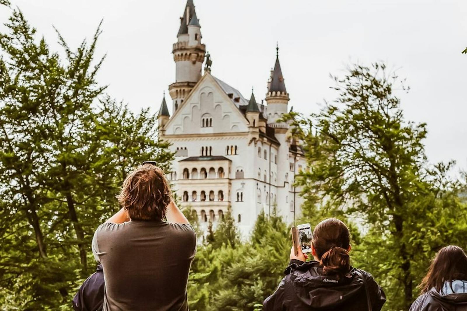 Vizitatori fotografiind Castelul Neuschwanstein din copaci